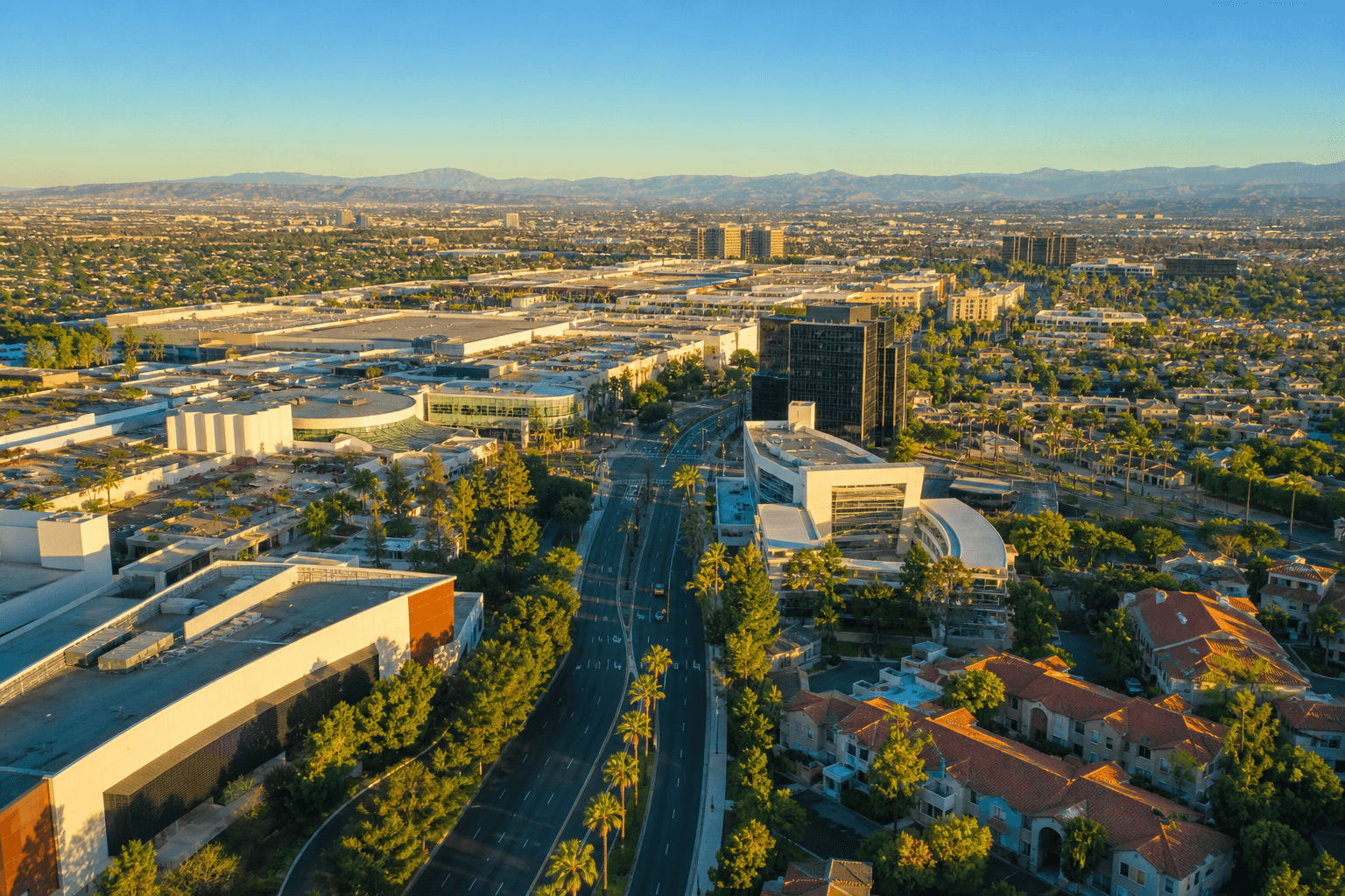 Aerial golden-hour view of Costa Mesa California — wide boulevards, palm trees, and the Orange County landscape stretching toward the coast
