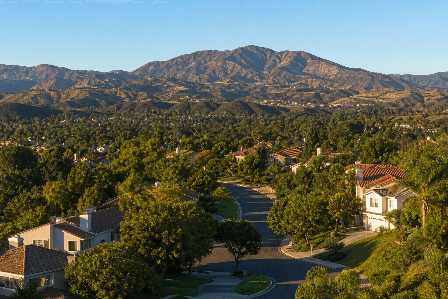 Suburban South Orange County landscape — quiet tree-lined streets, tile-roofed homes, and the Saddleback Mountains under a clear blue California sky